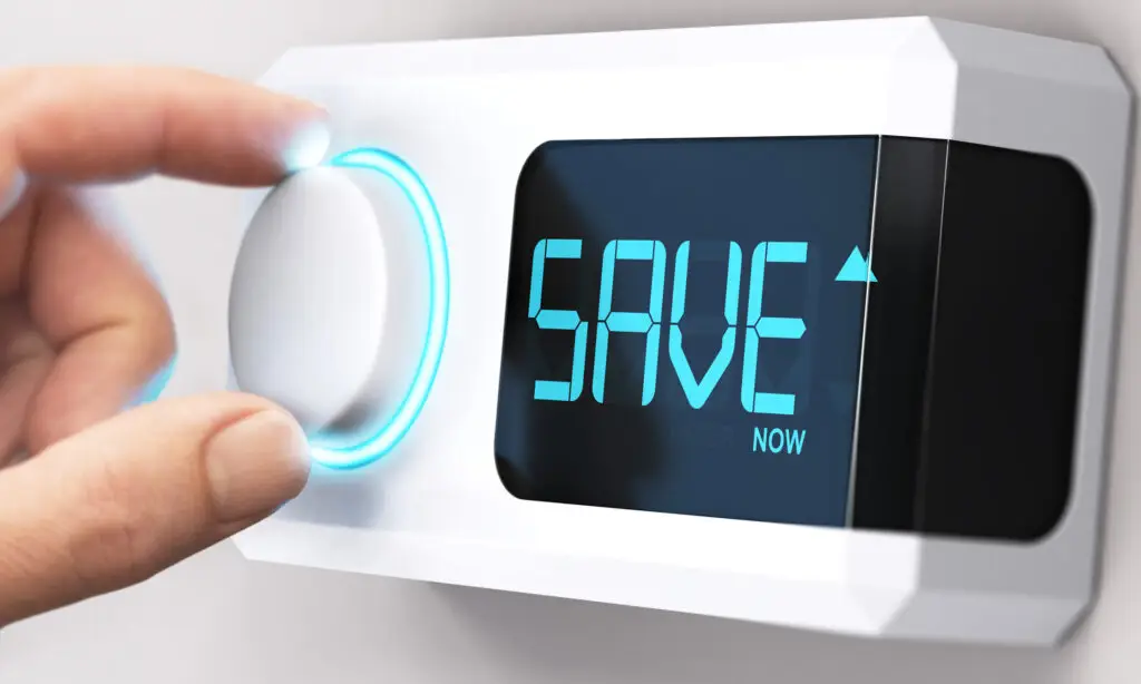 Close-up of a person's finger adjusting a thermostat dial displaying the word “SAVE” on screen.