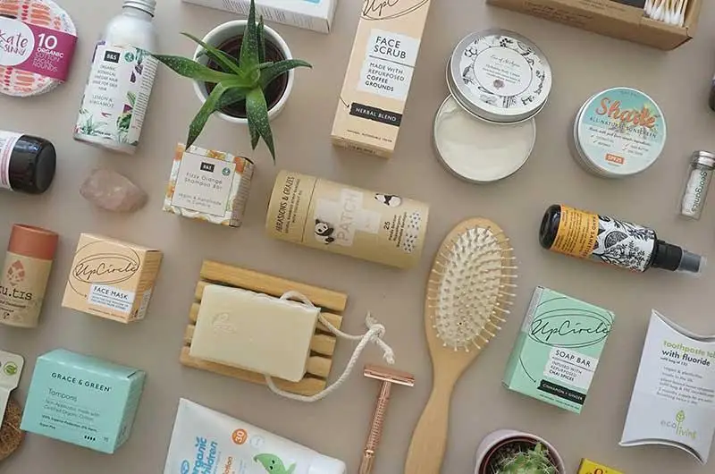 Flat lay of sustainable personal care and household products including soaps, creams, bamboo toothbrush, and reusable items.
