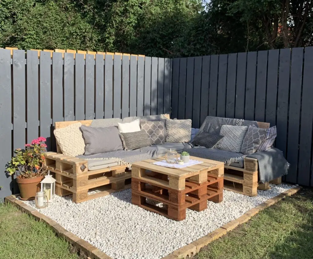 DIY outdoor lounge area featuring wooden pallet furniture with cushions and a pallet coffee table on white gravel.