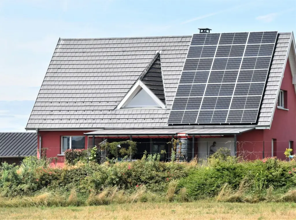 Modern house with a steep roof covered partially by large solar panel array and surrounded by greenery.