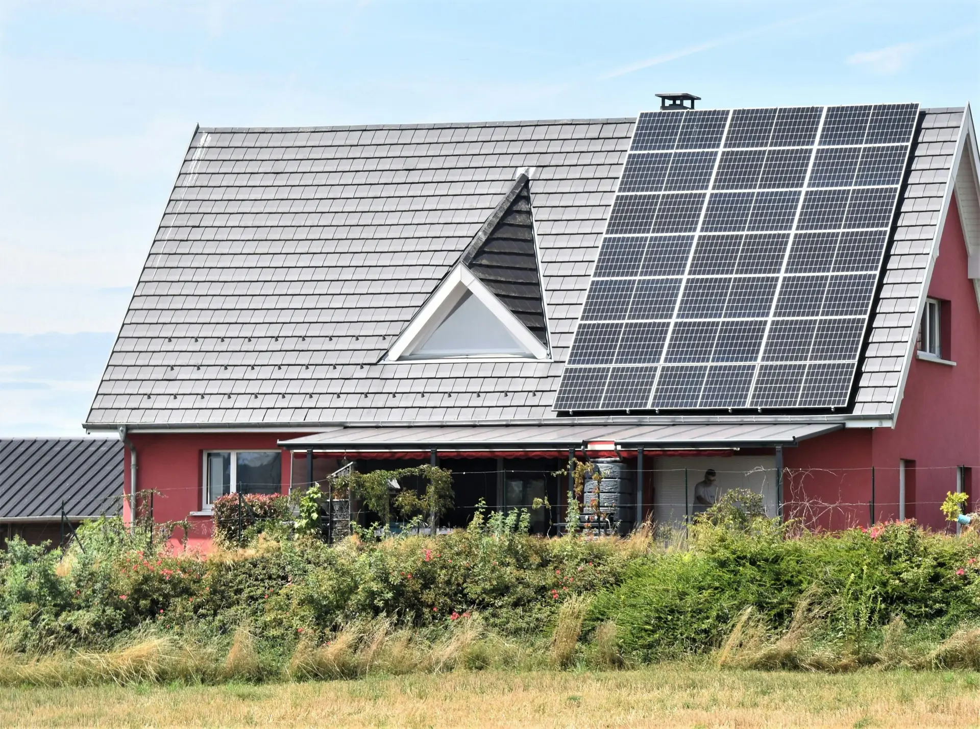 Modern house with a steep roof covered partially by large solar panel array and surrounded by greenery.