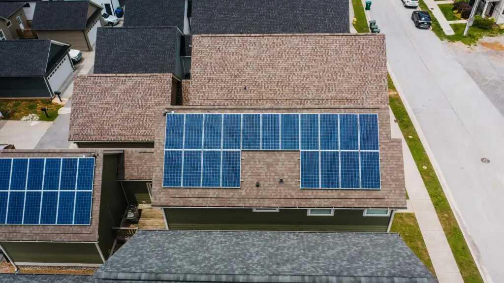 Aerial view of a residential neighborhood with houses featuring solar panels on their roofs, lining a quiet street.