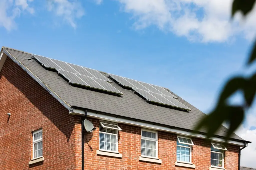 Rooftop solar panels installed on a brick house under a bright blue sky with scattered clouds.